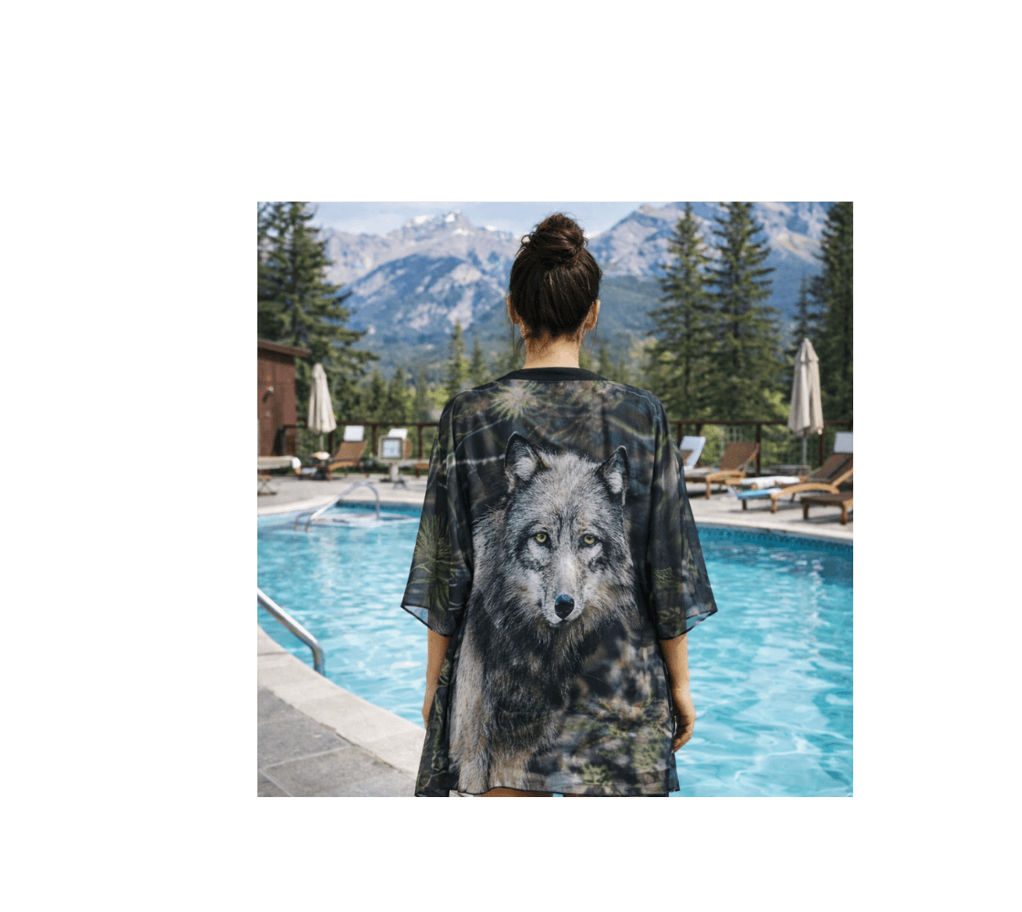 A Woman standing wearing a gray wolf kimono cover up from our real wildlife photography by a pool with mountains in the background.