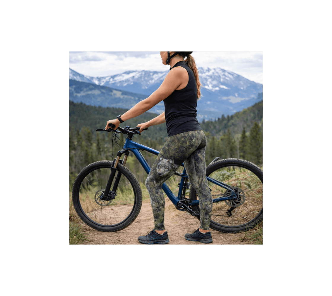 Waman wearing a pair of gray wolf yoga leggings from our real wildlife photography standing by mountain bike with mountain in the background.