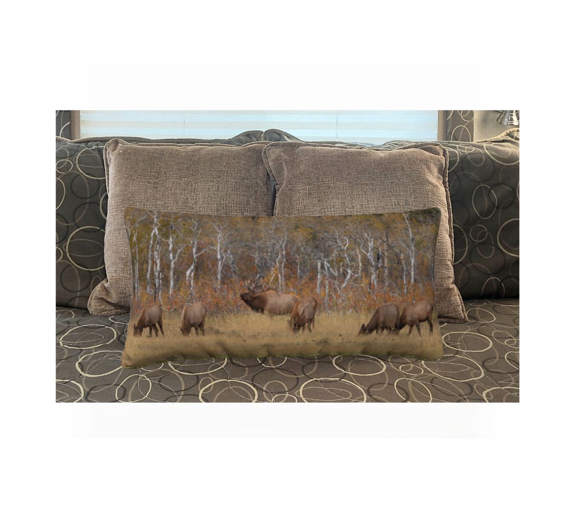 Decorative pillow with a nature scene of trees and elk on a bed.