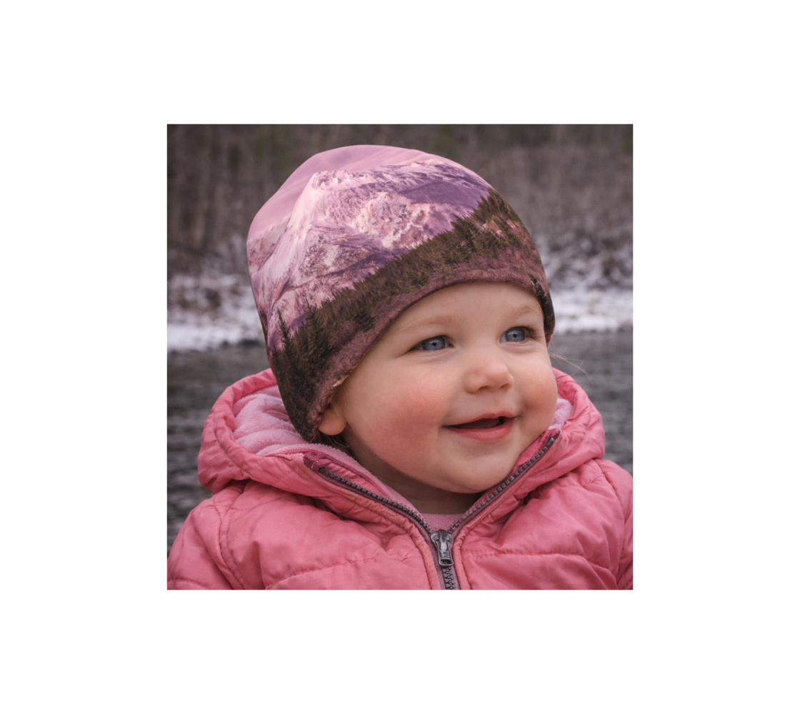 A toddler in nature wearing a bamboo-lined beanie with an image of pink mountain design.