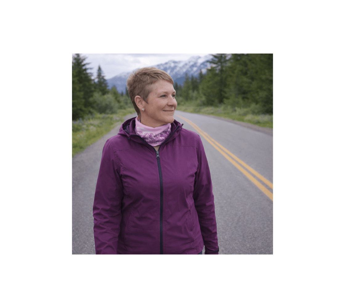 Woman standing on the side of a road  wearing a pink mountain sunset head and neck buff from our wildlife photography around her neck.
