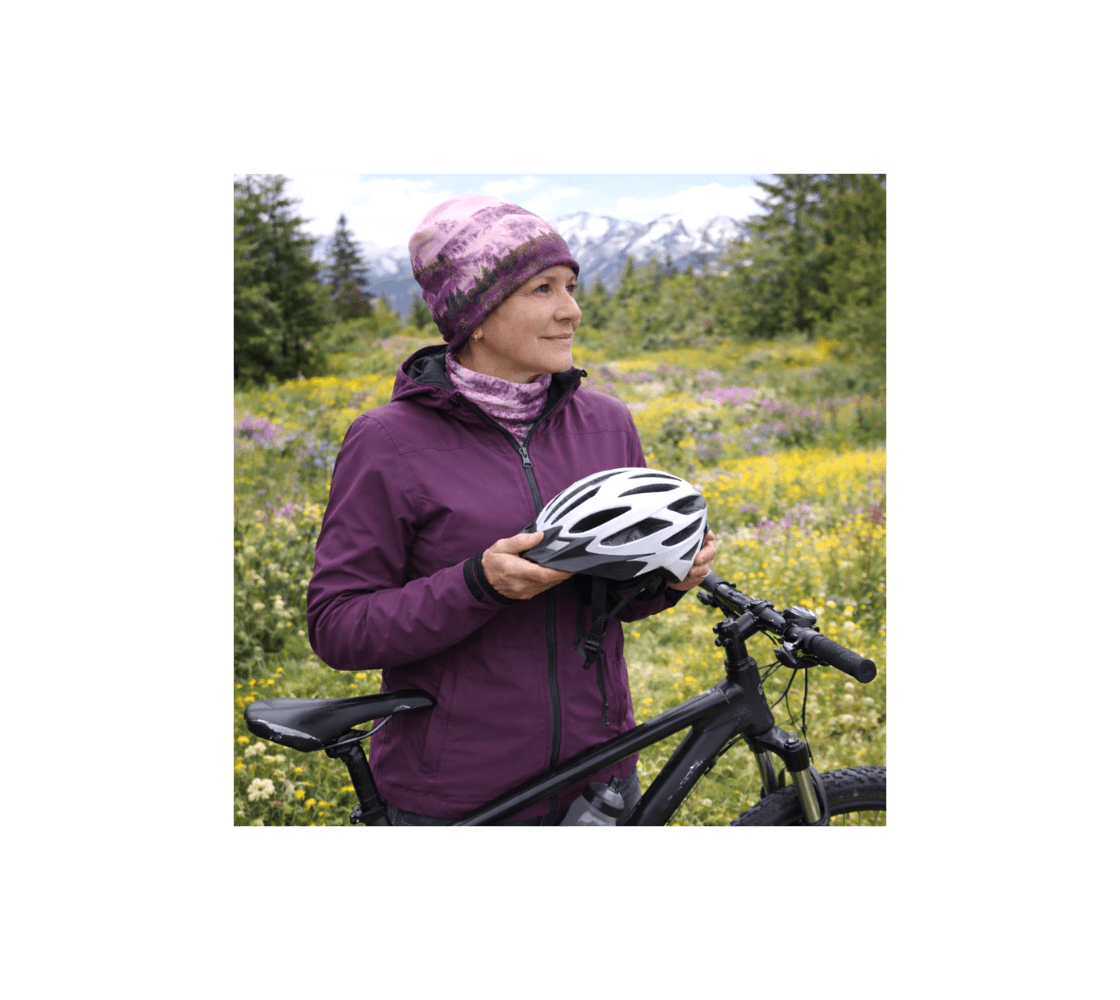 A woman standing by her bicycle wearing a pink mountain sunset beanie from our real nature photography.