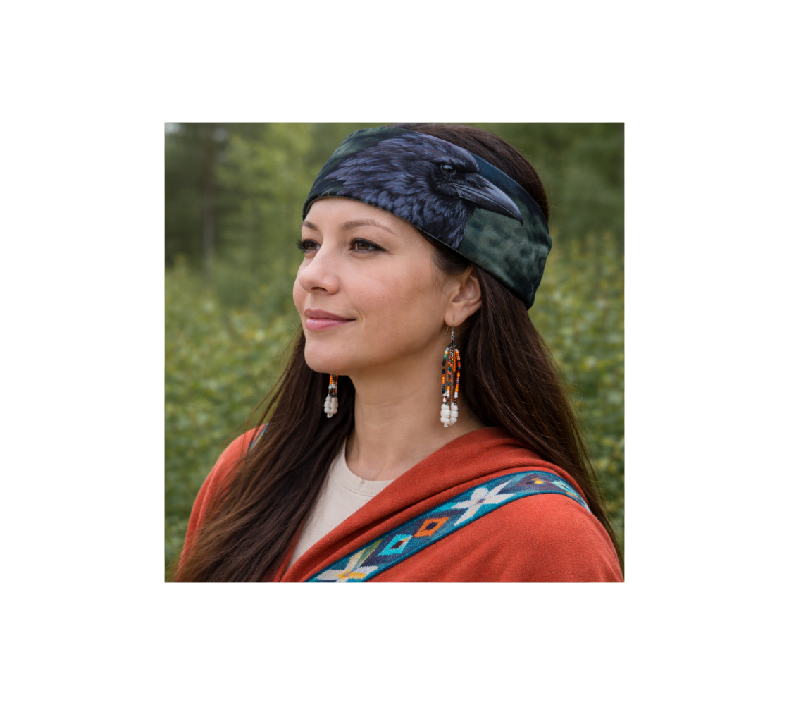 A Woman wearing a head and neck buff on her head with an image of a raven design with a mottled green background. 