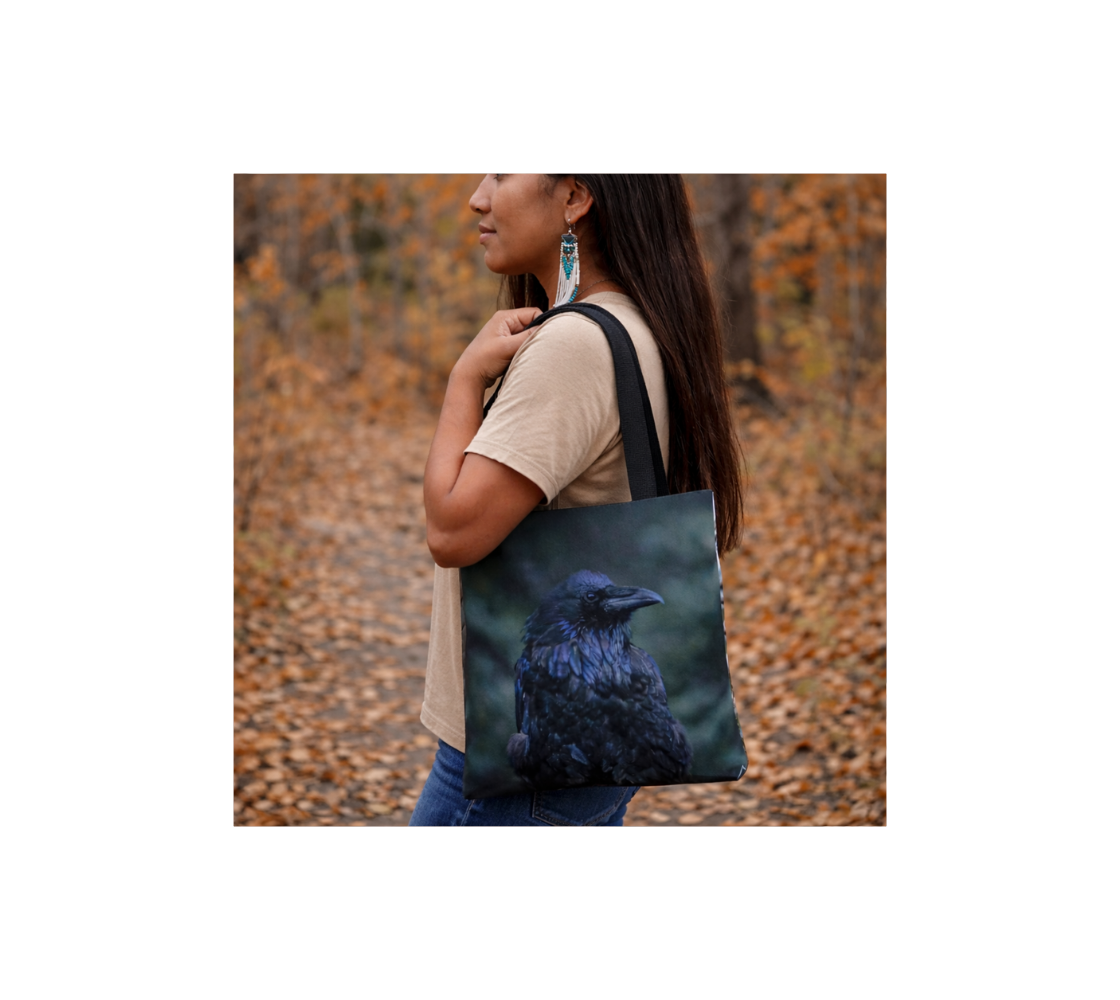 A woman carrying a small reusable tote bag with a portrait of a raven design with a mottle green background in an outdoor setting.