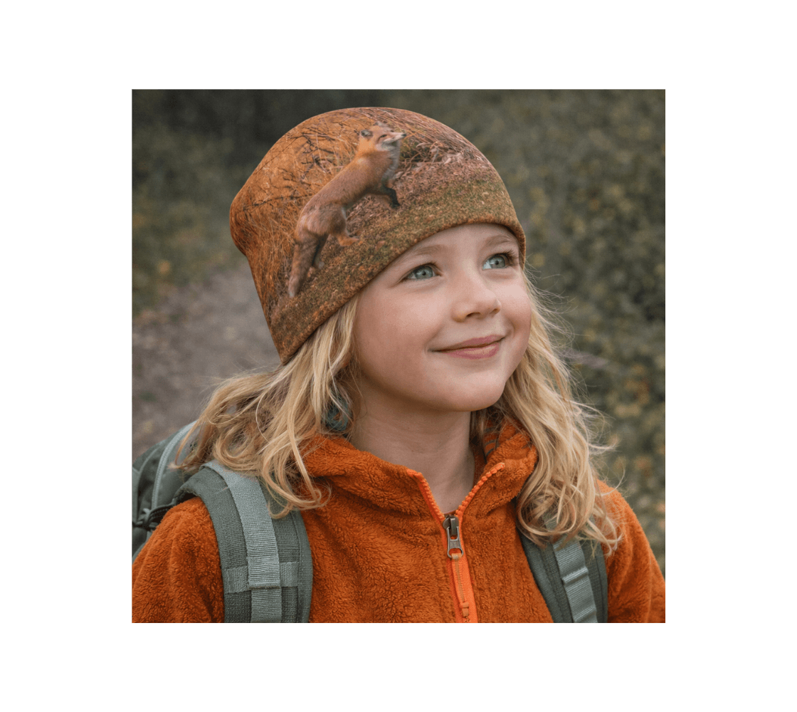 A young girl standing wearing a red fox bamboo-lined beanie from our real wildlife photography in a forest.