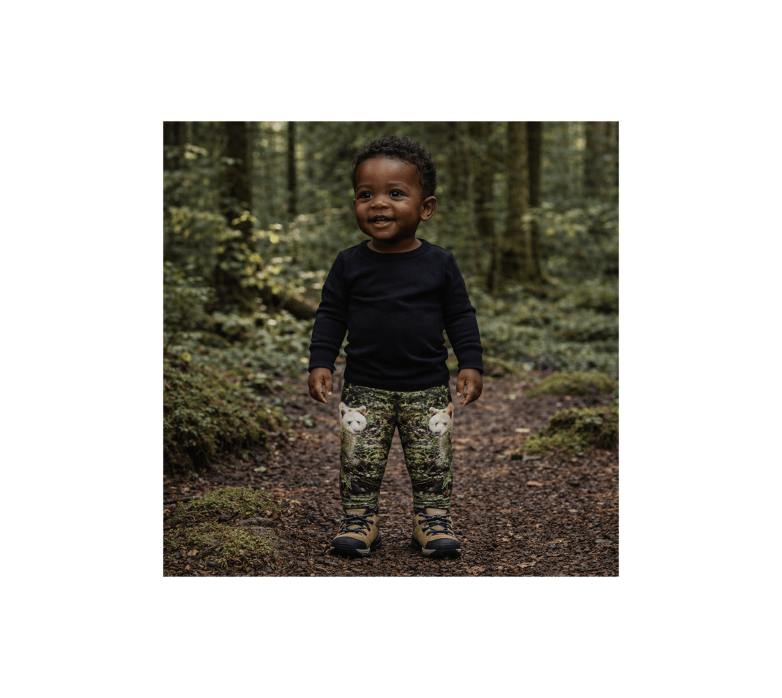 A young boy wearing a pair of spirit bear baby leggings from our wildlife photography standing in a forest.