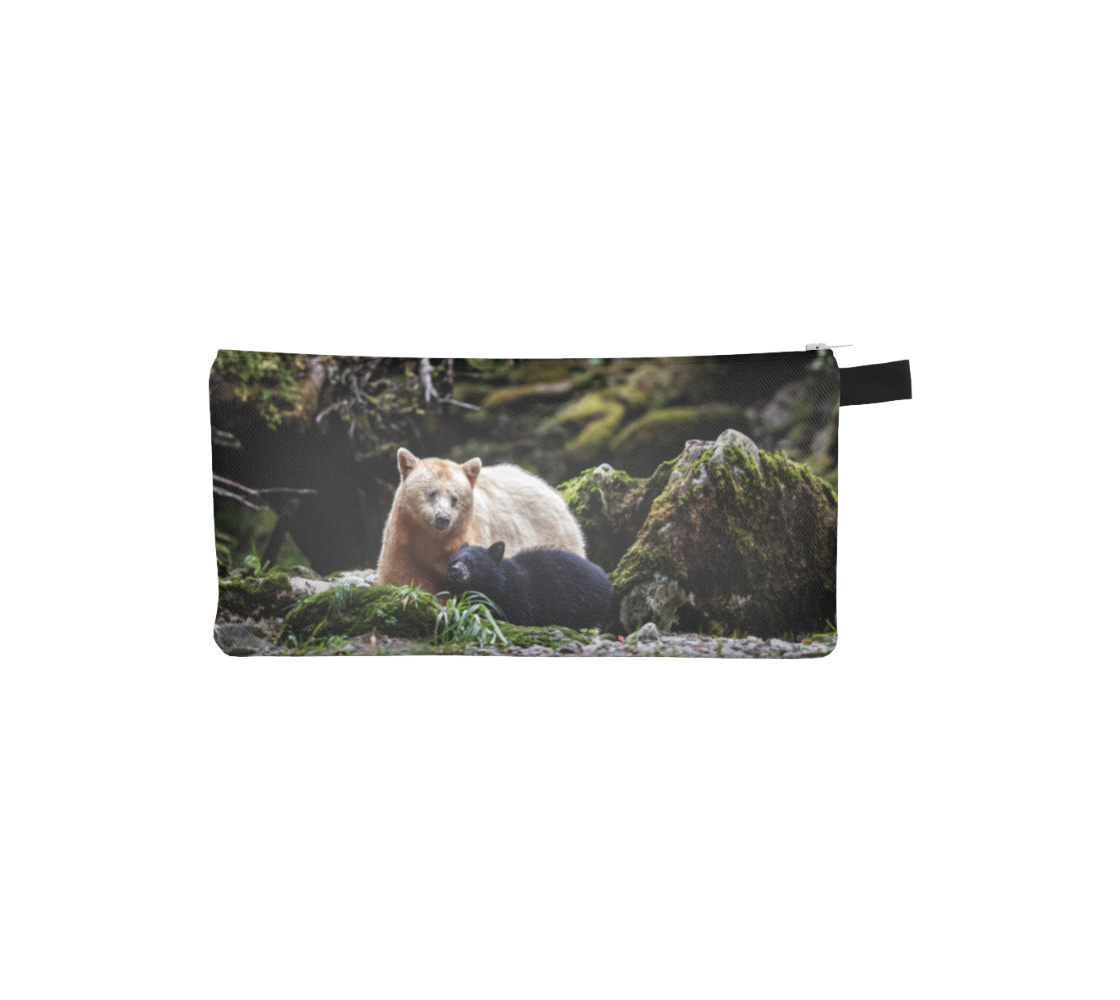 This images features a photo of a white mama spirit bear with her black bear cub beside her on a canvas zippered pouch. The background is grey rocks and tree roots covered in green moss. 