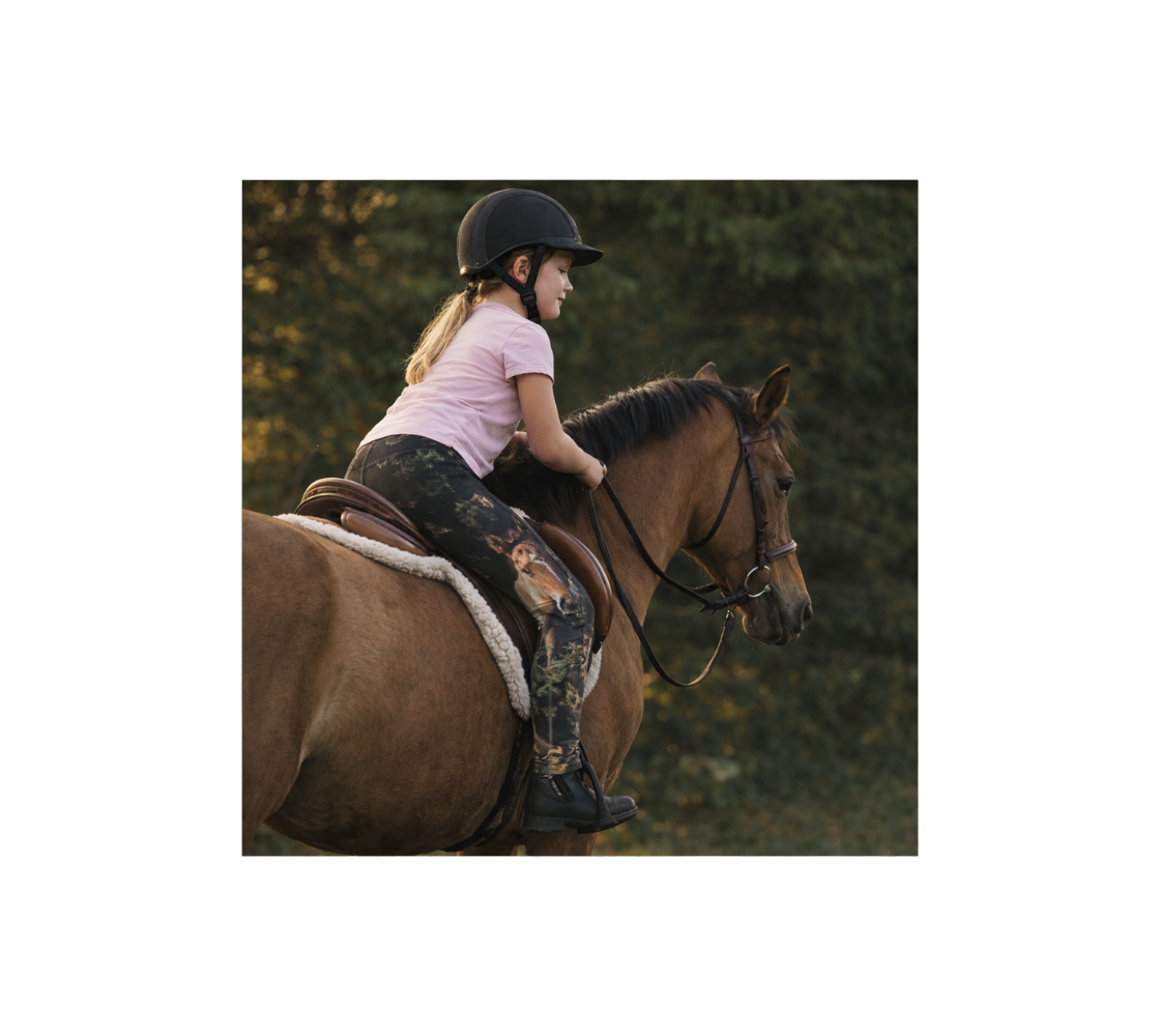 Youth riding a horse in an outdoor setting with a pair of leggings with a image of wild horses colts.
