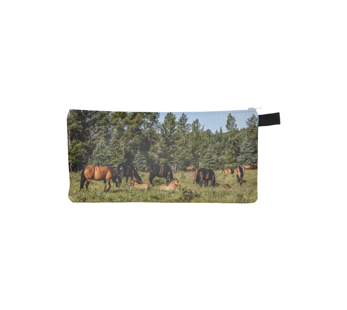 This image features a photograph of wild foals lying in wildflowers in the summer, with a herd of wild horses grazing in a field surrounded by trees, on a canvas zippered pouch. Color tones include greens, browns, and black.