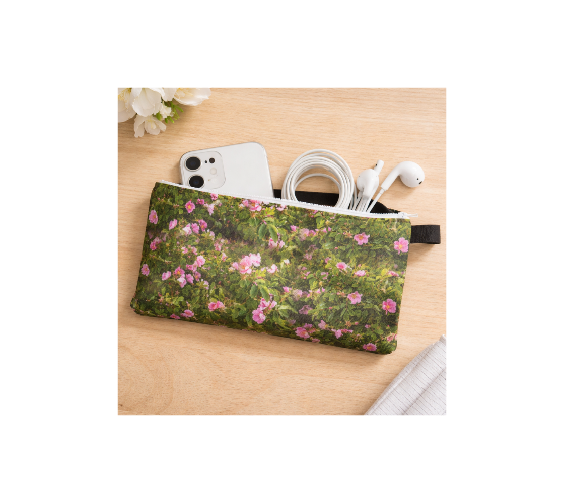 A zippered pouch with a collage of wild roses design with a green background with a phone, cable, and earphones inside it.