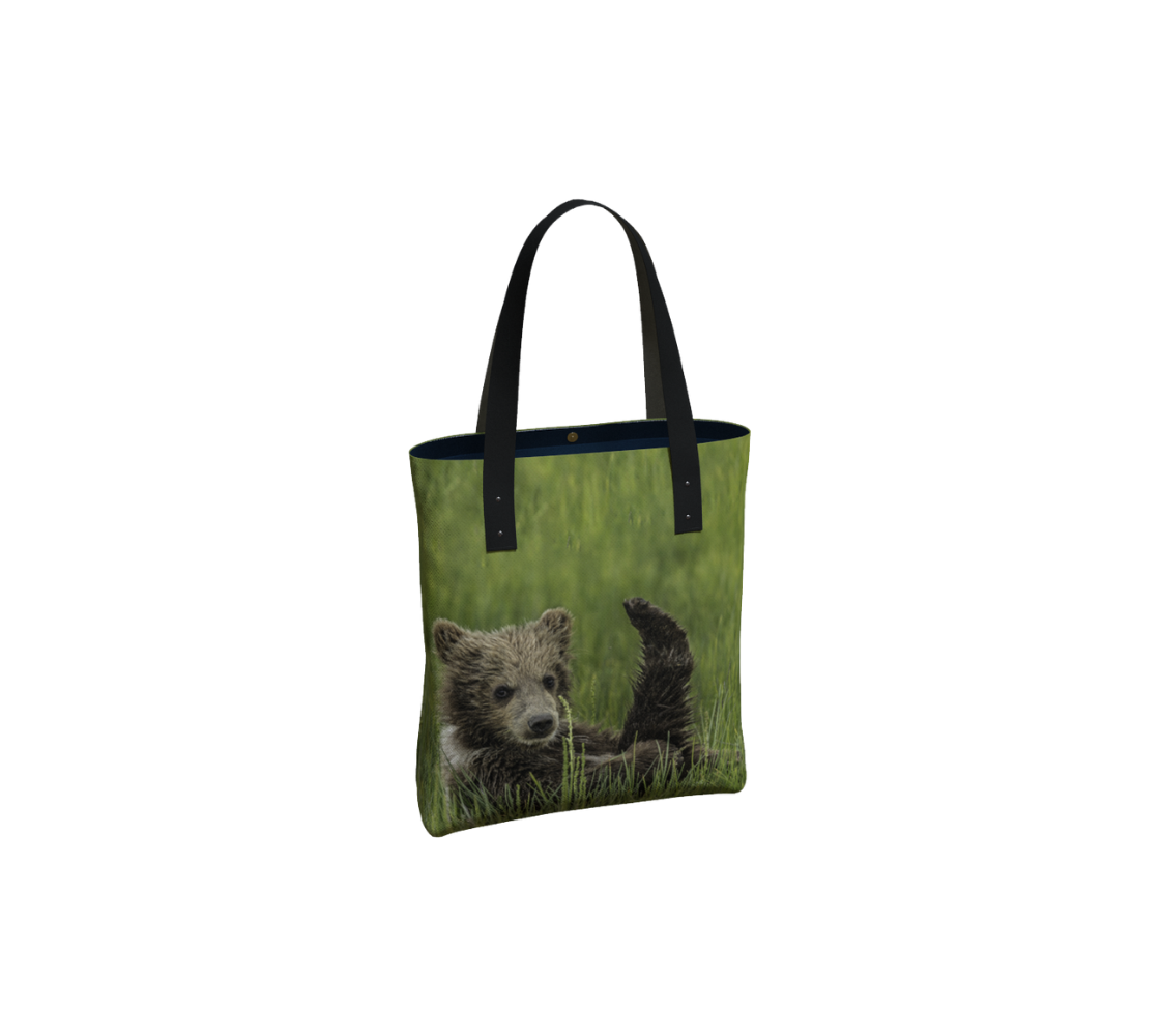 Durable canvas handbag with 1” vegan leather straps and magnetic closure with inside pockets. Features double sided real images grizzly bear cub with its leg in a yoga pose. Measures 16” x 13” x 3”.