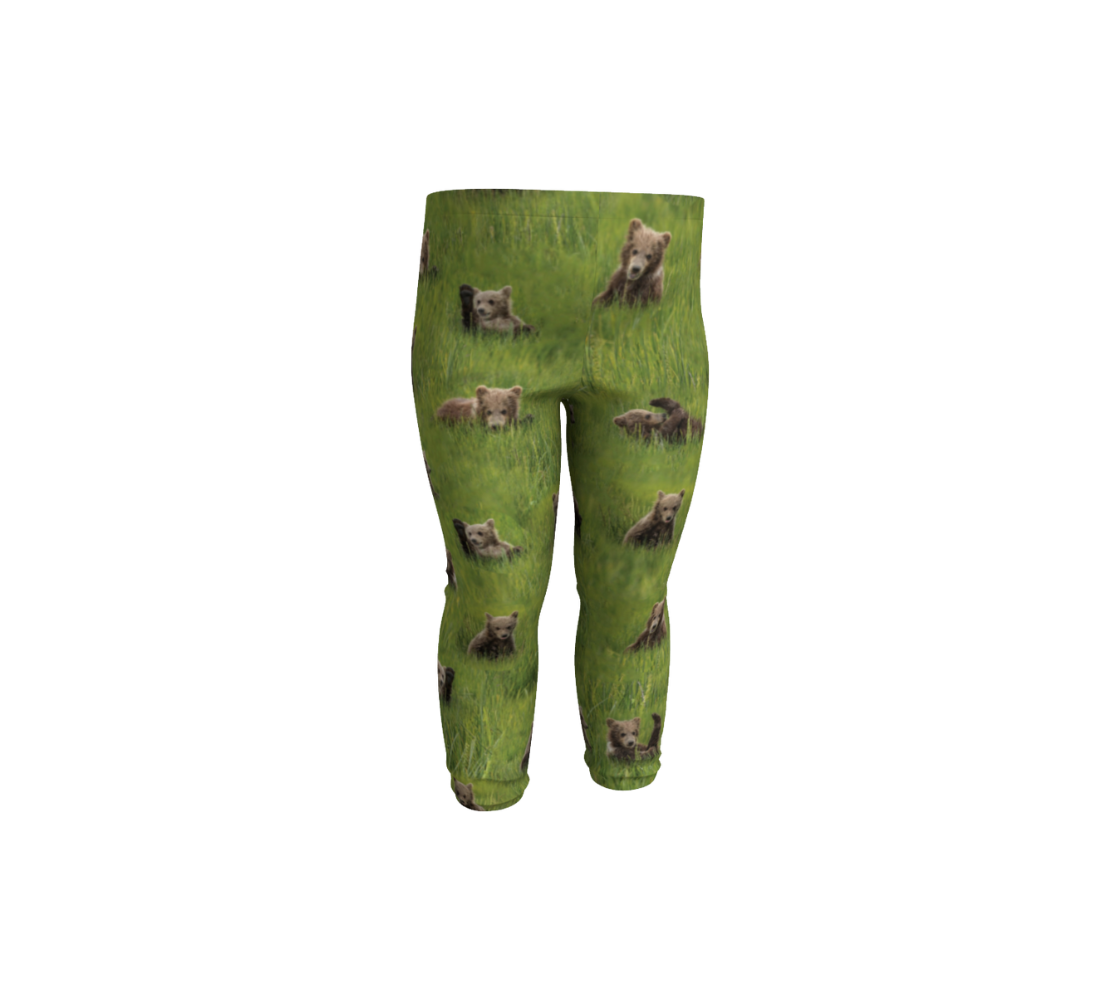 This is a front profile of a pair of infant leggings featuring a collage of photos of little bear cubs playing in the grass. The background is bright green grass with little light brown colored bear cubs scattered throughout the leggings.