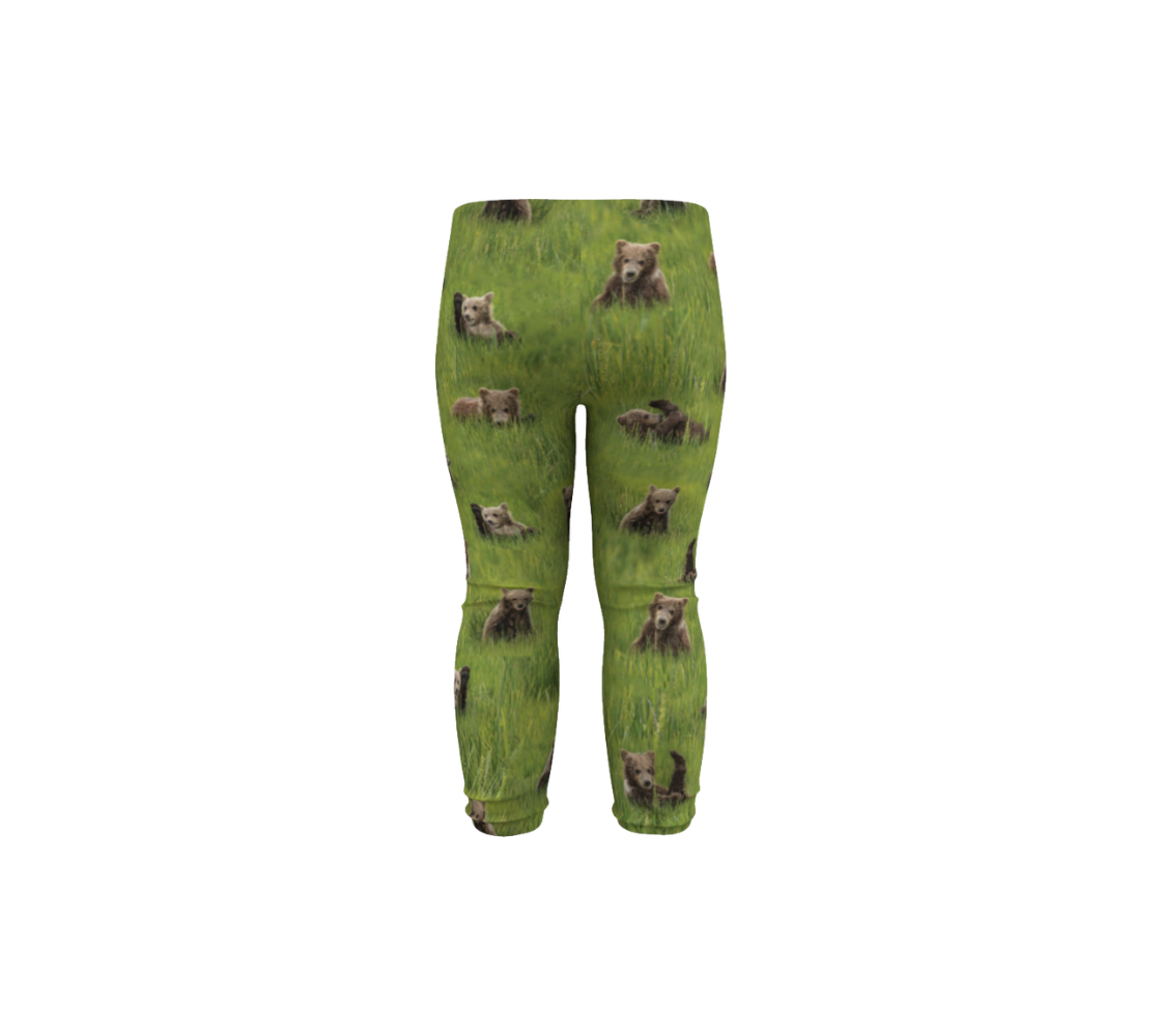 This is a rear profile of a pair of infant leggings featuring a collage of photos of little bear cubs playing in the grass. The background is bright green grass with little light brown colored bear cubs scattered throughout the leggings.