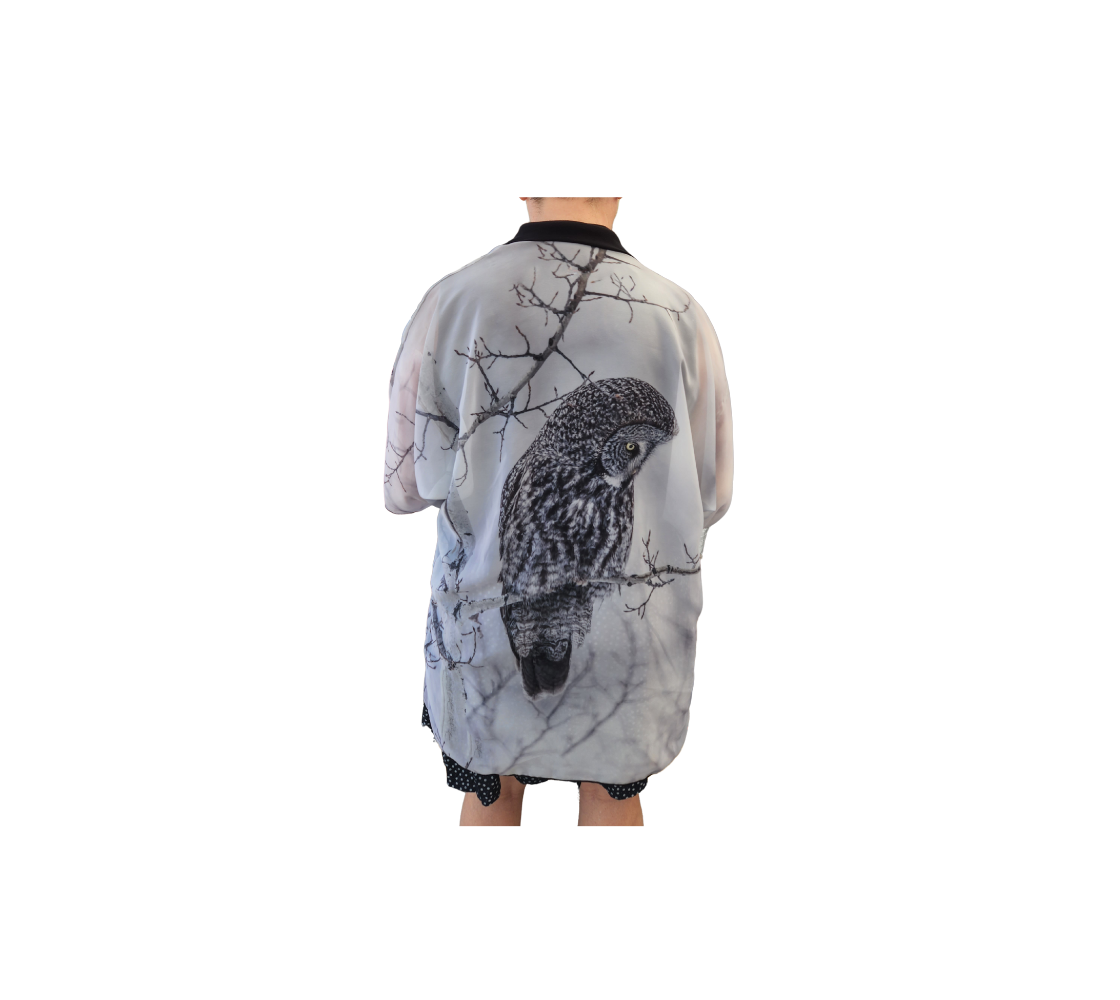 This is a backview is a lady wearing a semi-sheer poly chiffon kimono robe featuring a photo of an owl. Background is white and grey with blurred tree branches due to the fog and frost at the time, with a great grey owl sitting on a branch looking downward. Kimono has black lightweight bamboo trim.