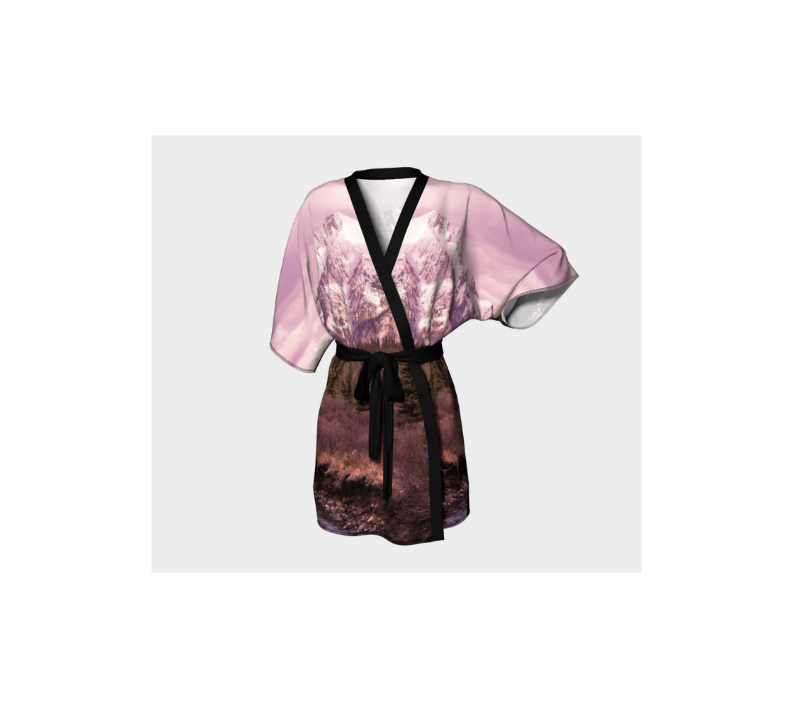 This frontview is a semi-sheer poly chiffon kimono robe featuring a photo of a mountain scene. The background is a pink mountain sunset scene, with pine trees and a creek running along the bottom. Kimono has black trim and a black lightweight bamboo belt for tying.