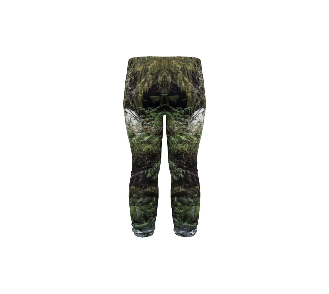 This is a rear profile of a pair of infant leggings featuring a photo of a spirit bear on the side of each leg. The background is green bushes and brown branches of the Great Bear Rainforest. The white spirit bear is stepping down out of the forest and is making her way to the stream below. 