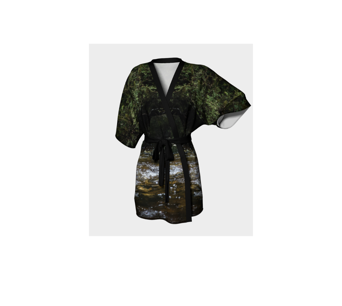 The frontview is a semi-sheer poly chiffon kimono robe featuring a photo of creek and forest. The background is  of green trees and moss with a gold  and green colored creek. Kimono has black trim and a black lightweight bamboo belt for tying.