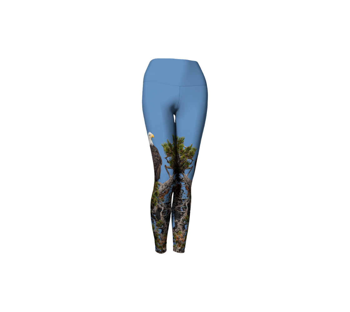 This is a front profile of a pair of yoga leggings featuring a bald eagle on the side of each leg, with a 4.5 inch high waist band. The background is a blue sky with a bald eagle perched on top of a pine tree. 