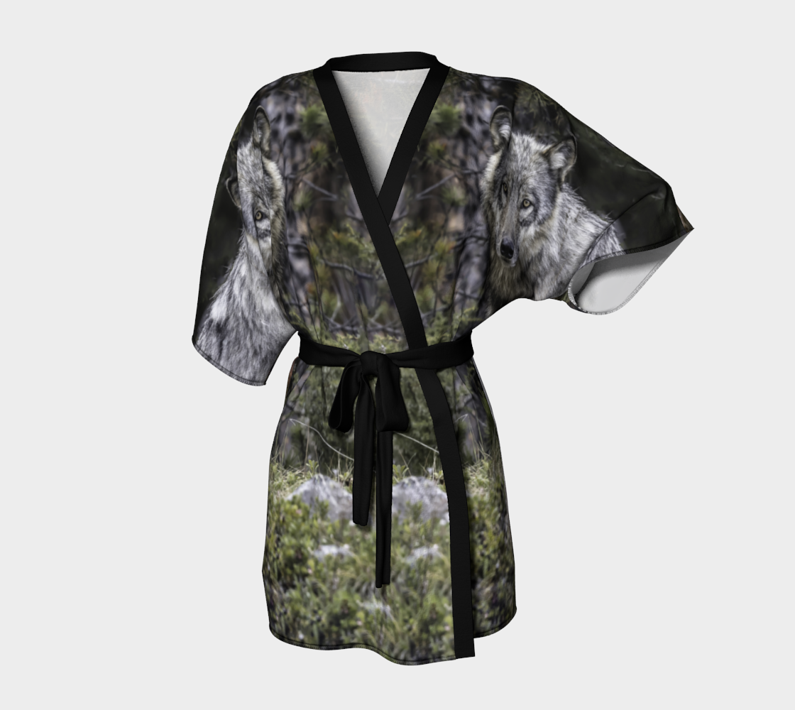 This frontview is of a semi-sheer poly chiffon kimono robe featuring a photo of a wolf. Background is green and grey with pine tree branches with a, grey wolf head image on each shoulder. Kimono has black trim and a black lightweight bamboo belt for tying.